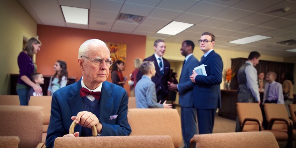 A young brother observes an elderly brother sitting alone in the Kingdom Hall