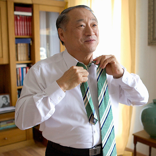 An older man putting on a tie