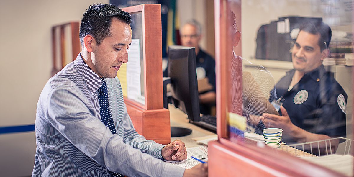 A Christian man fills out documents as government officials look on
