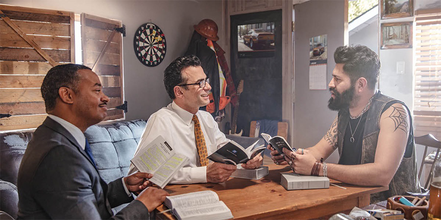 Two brothers conduct a Bible study with a man who has many tattoos and is wearing bracelets and necklaces