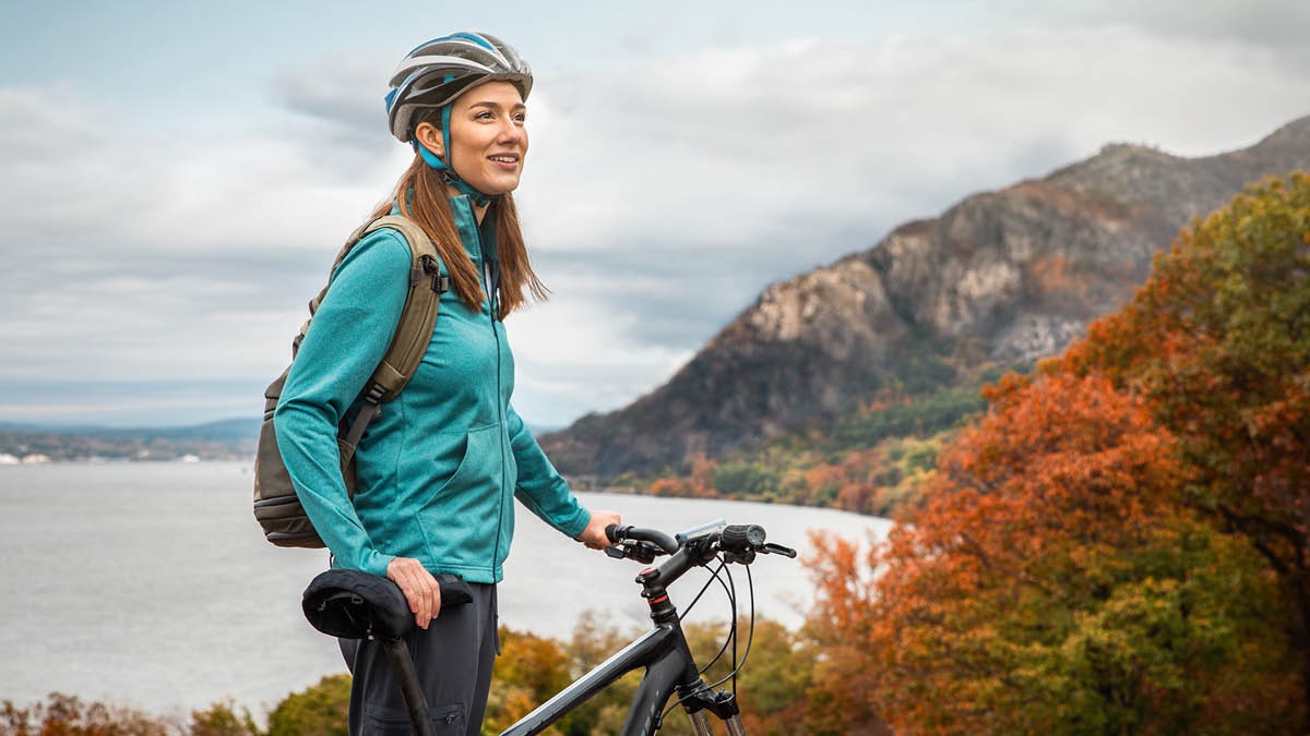 A sister riding a bike stops atop a hill overlooking a lake to enjoy creation.