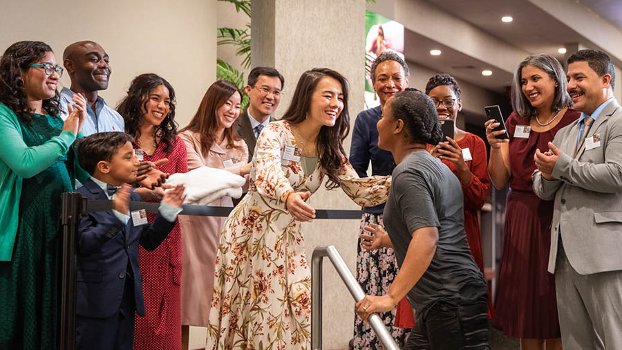 The Bible student stepping out of the baptismal pool. Her husband, the sister who studied with her, and several others from the congregation smile and applaud.