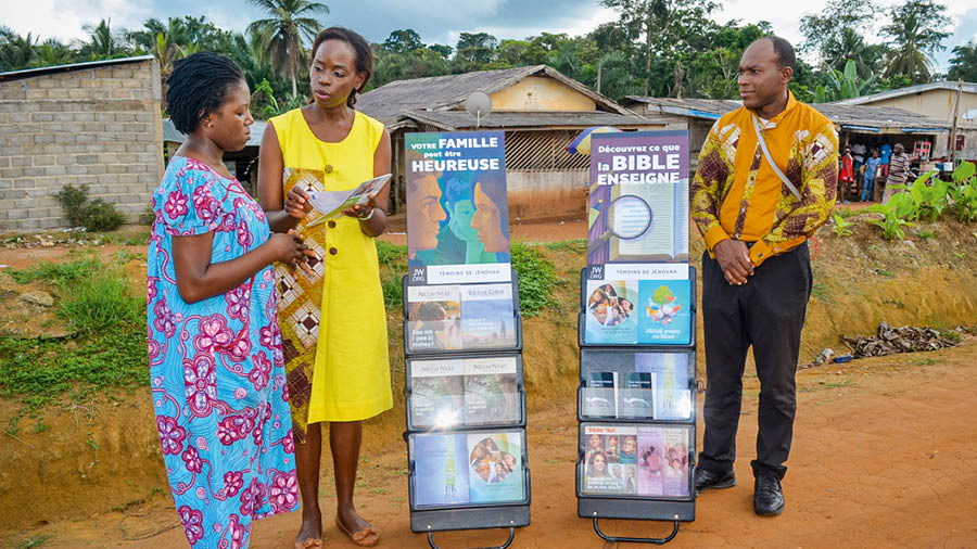 Stéphanie and Alain standing next to literature carts, preaching to a woman.