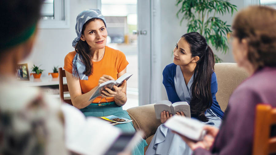 A sister conducting a meeting for field service. She is seated and wearing a head scarf.