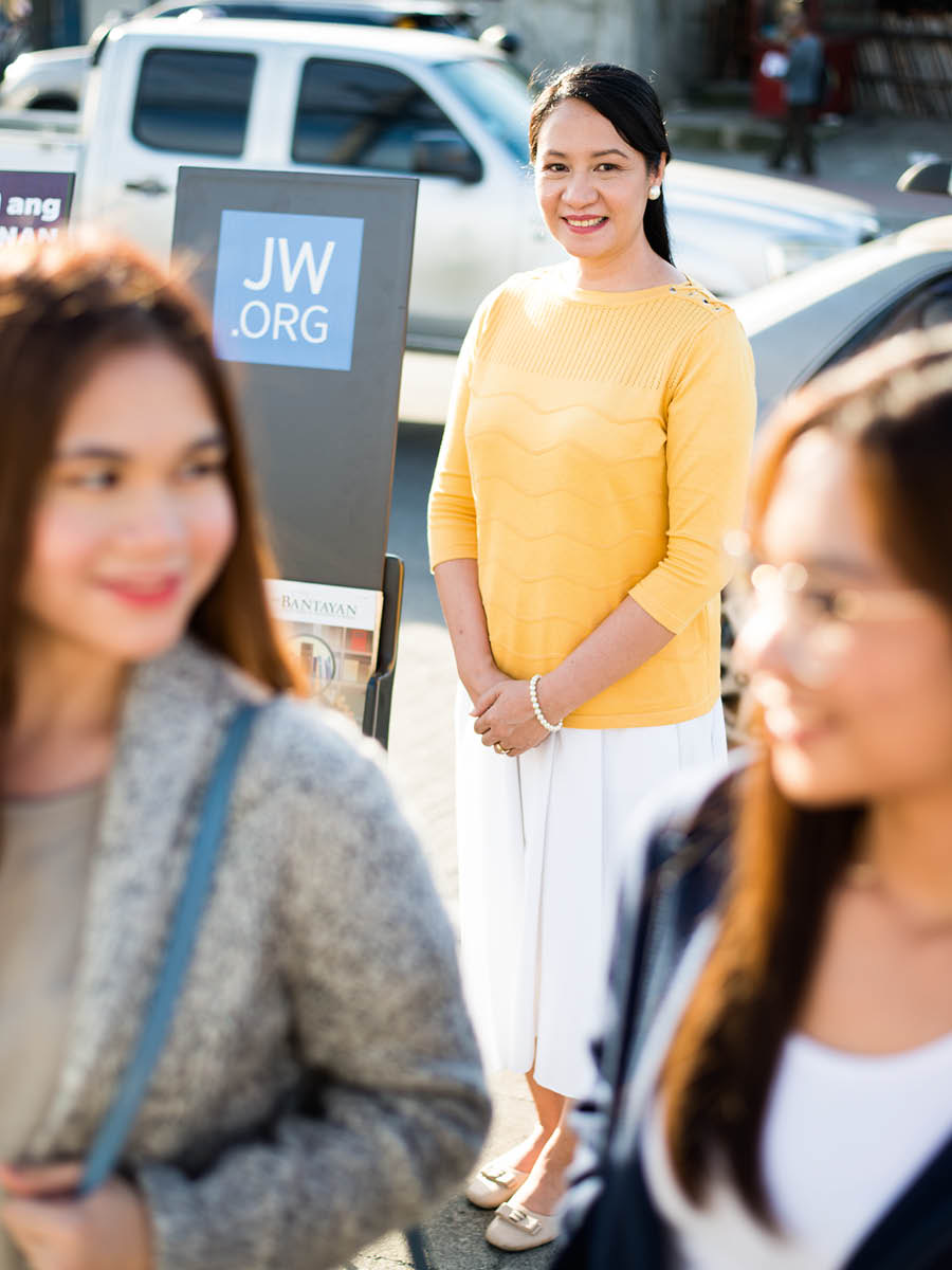 Helen smiling as she stands next to a literature cart. Two women walk by.