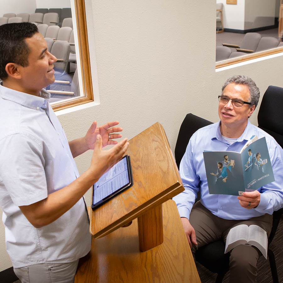 An elder listening to a brother practice a talk. The elder holds an open “Teaching” brochure.