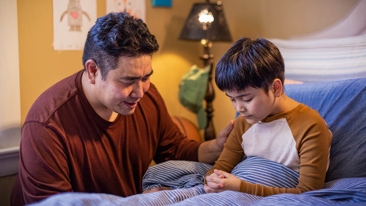 A father praying with his young son at bedtime.