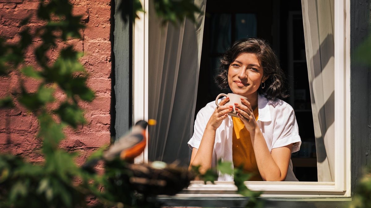 A sister happily observing a bird from a window.