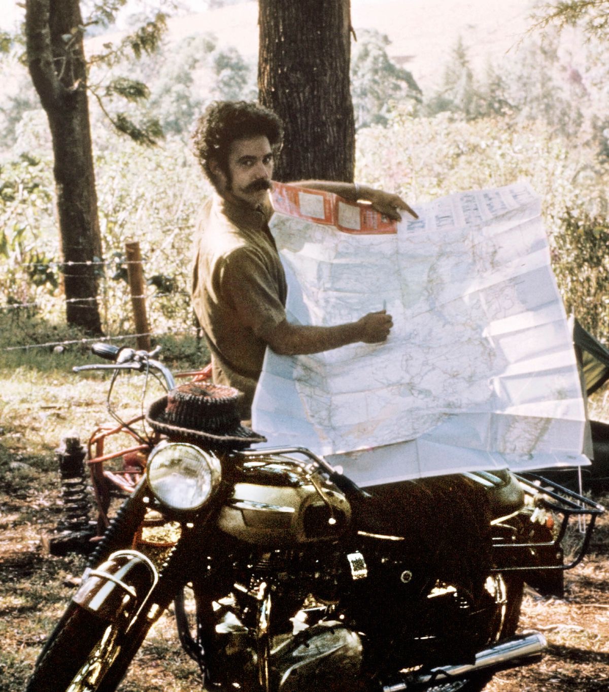 Robert standing by his motorcycle and showing a map of his travels.