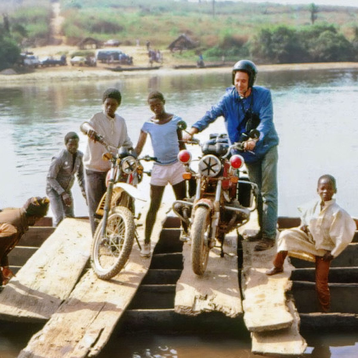 Robert and others with their motorbikes, crossing a river on a log raft.
