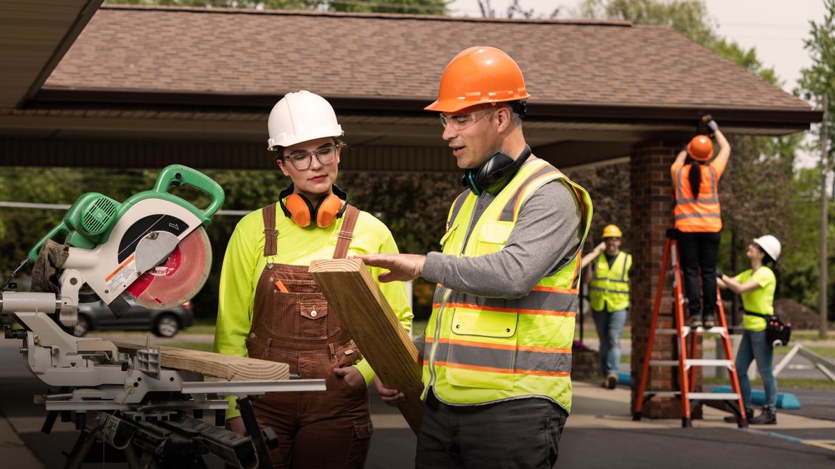 A brother training a sister to operate a power saw at a Kingdom Hall construction project.