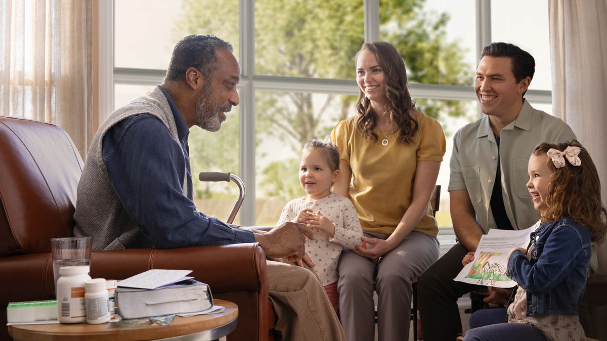 The elderly brother shown in the previous image, sitting in his home in the springtime and warmly conversing with a couple and their two young daughters. Beside him is a cane and a few bottles of medication. One of the daughters is showing him her drawing of Paradise.