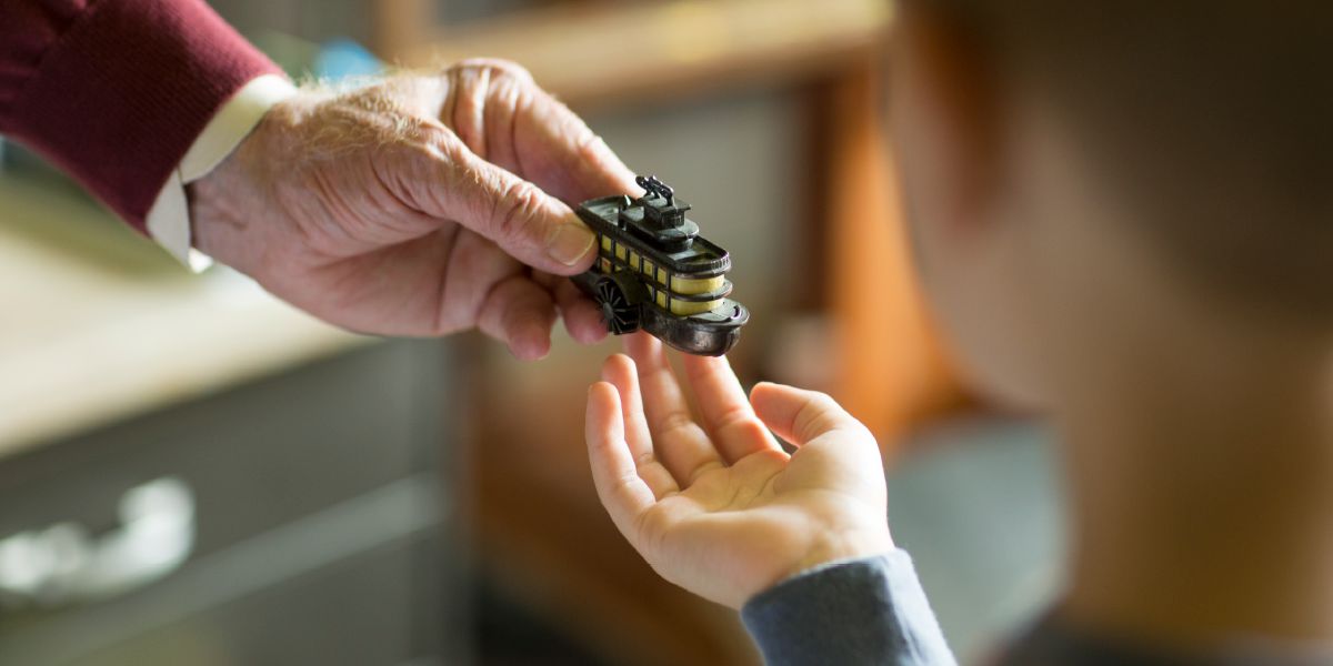 An elderly man gives a little boy a boat-shaped pencil sharpener