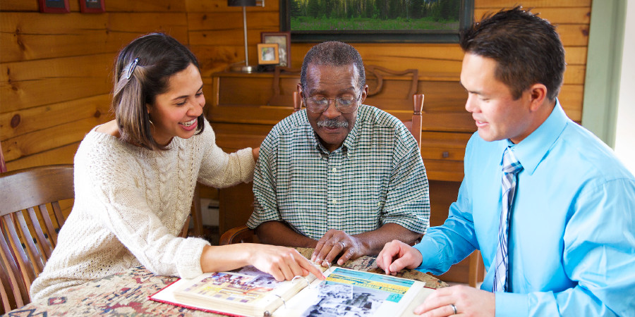 A couple and an older man reminisce as they look through a photo album
