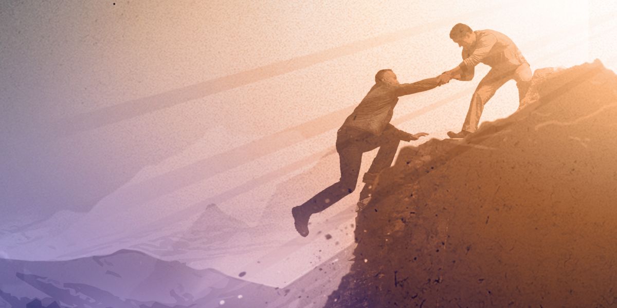 As a man starts to fall off a cliff, another man grabs his hand and pulls him to safety