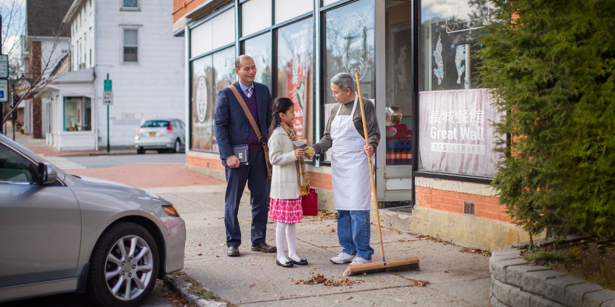 A father accompanies his daughter as she offers a tract to a person on the street