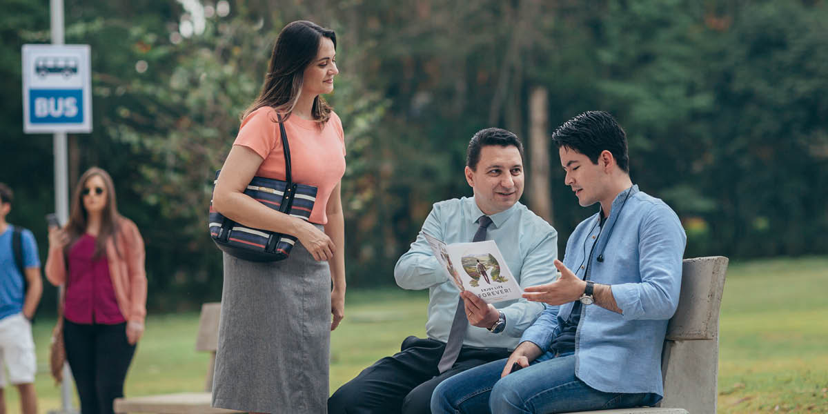 Un matrimonio usa el folleto “Disfrute de la vida” para hablar con un joven en una parada de autobús.