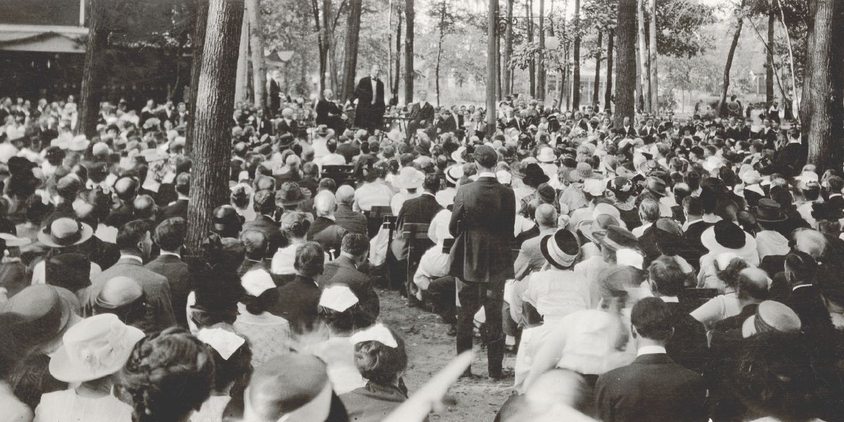 Joseph Rutherford hablando ante una multitud sentada bajo los árboles en la asamblea de los Estudiantes de la Biblia de 1919.