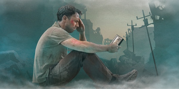 Assis sur des décombres, un homme anéanti regarde une photo