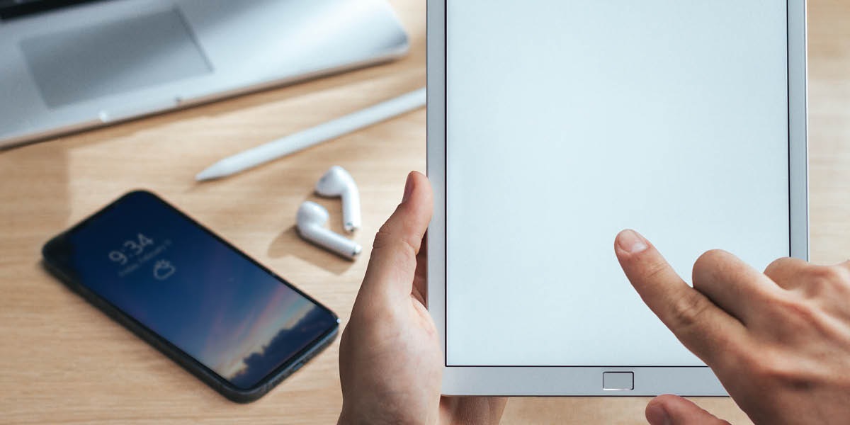 Quelqu’un en train d’utiliser une tablette. Disposés sur une table se trouvent d’autres appareils numériques.