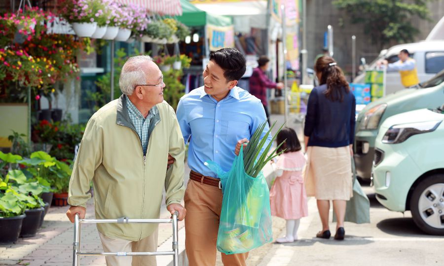 Un homme âgé marche avec un déambulateur et est aidé par un jeune homme