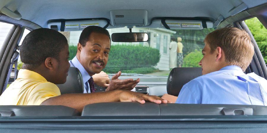 Un irmán maduro falando con dous irmáns novos sentados nun coche.