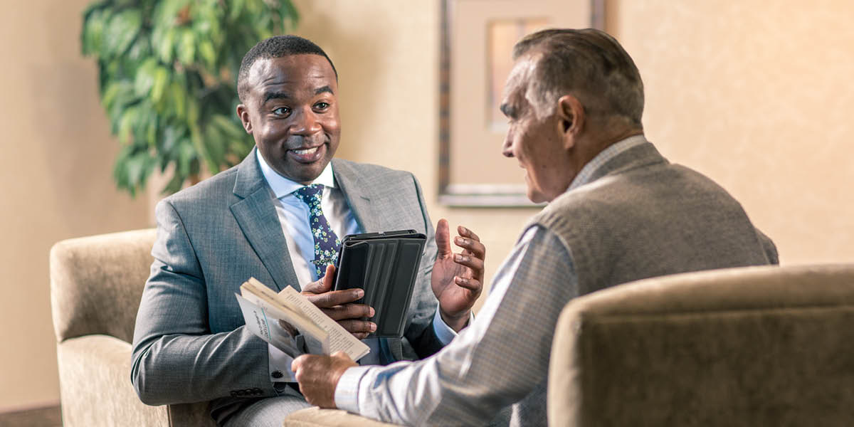 Un irmán sorrindo e facendo xestos mentres estuda a Biblia cun home maior