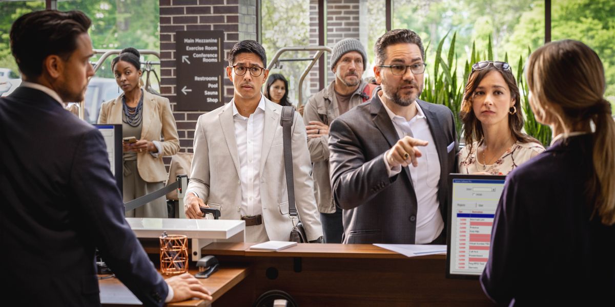 Peteĩ karai ipochy ha iñeʼẽ arhél peteĩ rresepsionísta ombaʼapóvape peteĩ otélpe. Pe karai rapykuéri oĩ heta kliénte ohaʼarõva pe fílape.