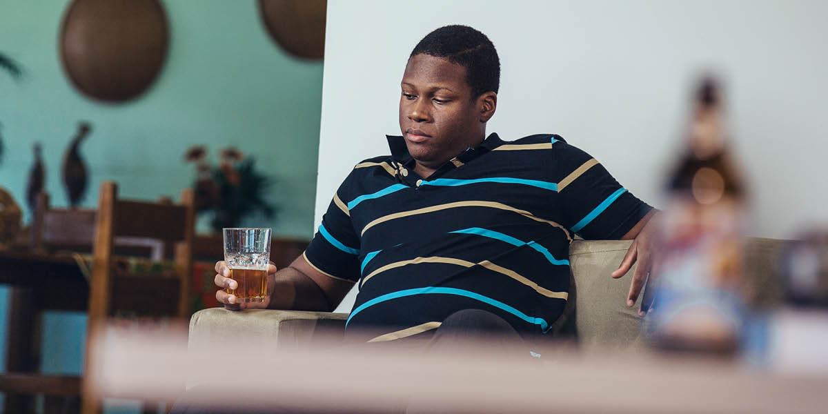 Yon mesye ki chita poukont li lakay li, l ap gade yon vè ki gen byè ladan l.