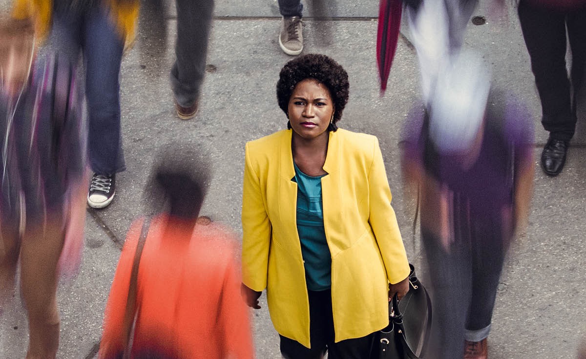 A woman standing on a street as people are walking by. She is looking up as if asking, ‘Does God notice me?’
