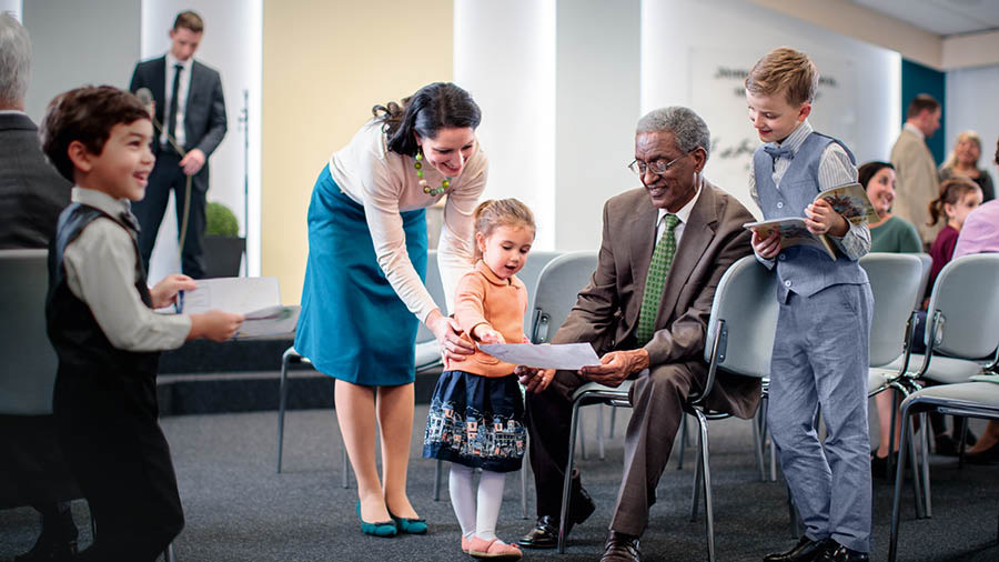 An older brother talking with young children at the Kingdom Hall and looking at pictures they have drawn.