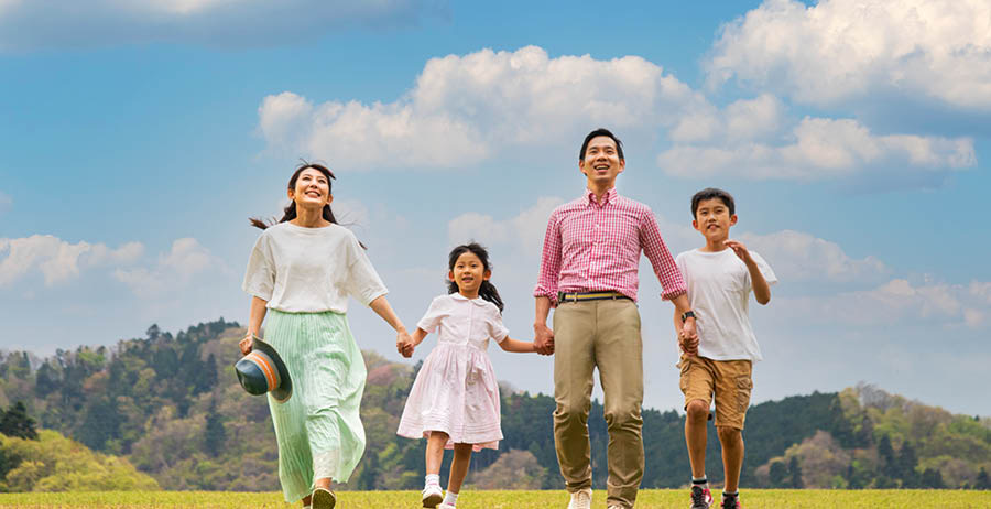 Parents holding hands with their two children as they walk happily through a field.