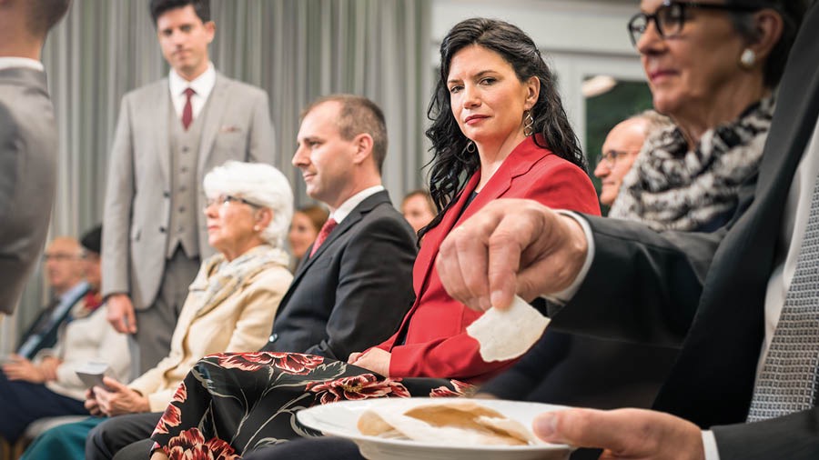 Systir fylgist athugul með bróður sem neytir brauðsins á minningarhátíðinni.
