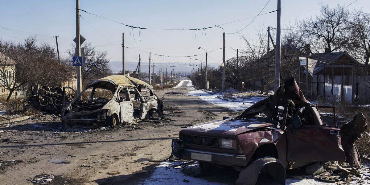 cnt_01: Carcasse di veicoli colpiti dalle bombe su una strada deserta in un villaggio ucraino distrutto.