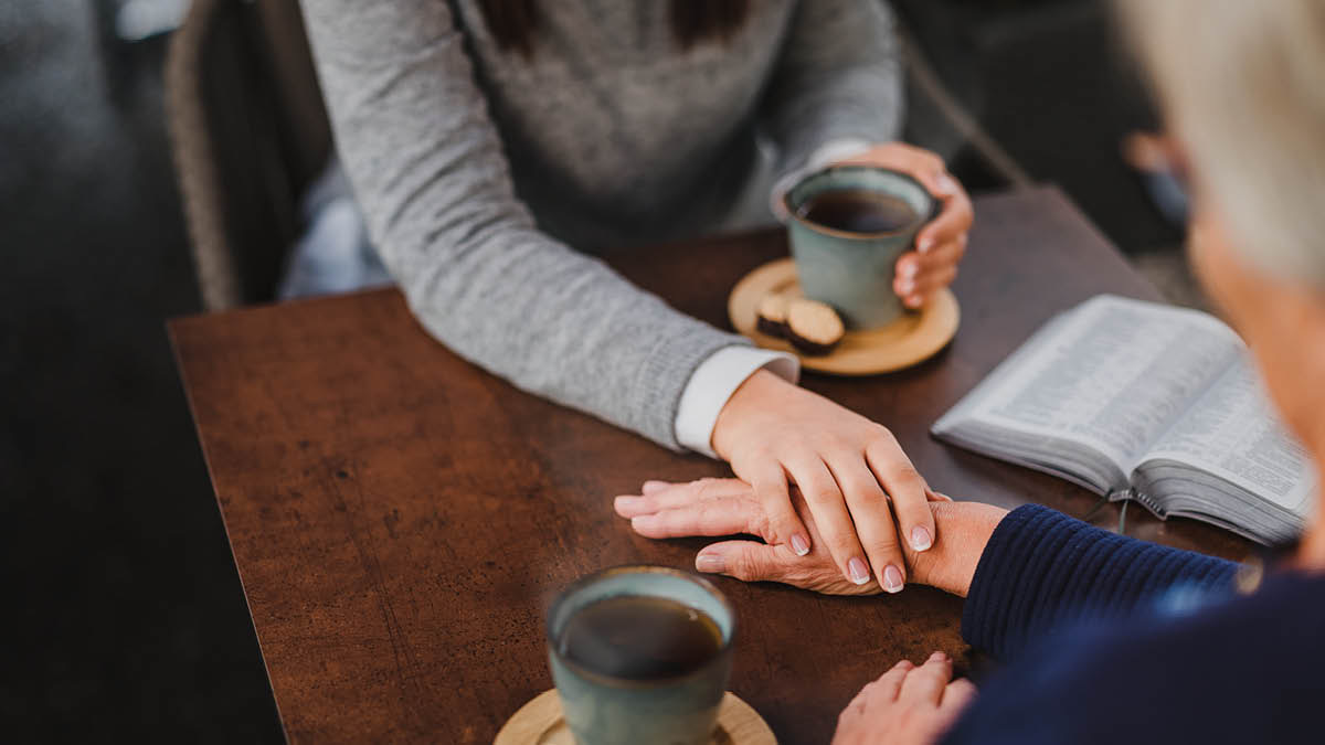 Una donna giovane tiene teneramente la mano di una donna più anziana.