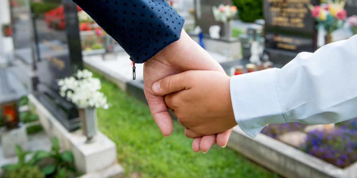 In un cimitero un bambino tiene per mano un adulto