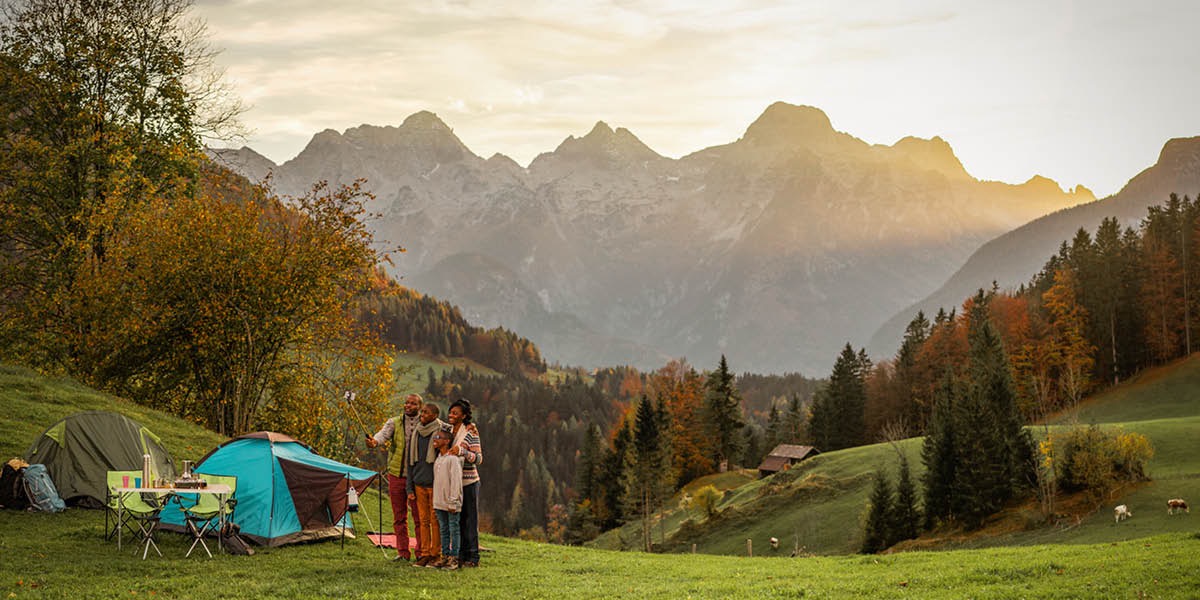 Una famiglia è in campeggio in montagna. La famiglia si fa un selfie con le montagne sullo sfondo.