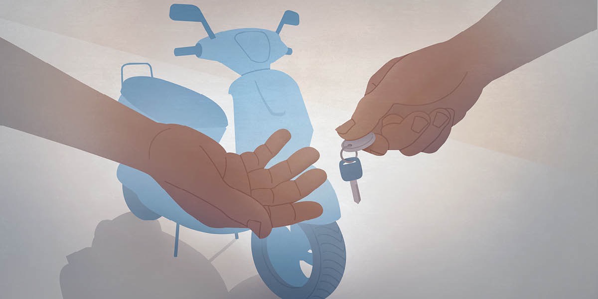 Il venditore di una moto consegna le chiavi all’acquirente. Sullo sfondo si vede la moto.