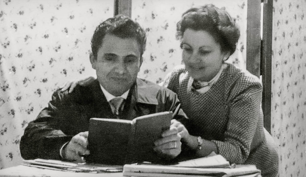 Antonio e Dorina leggono insieme davanti al paravento che separa gli ambienti.