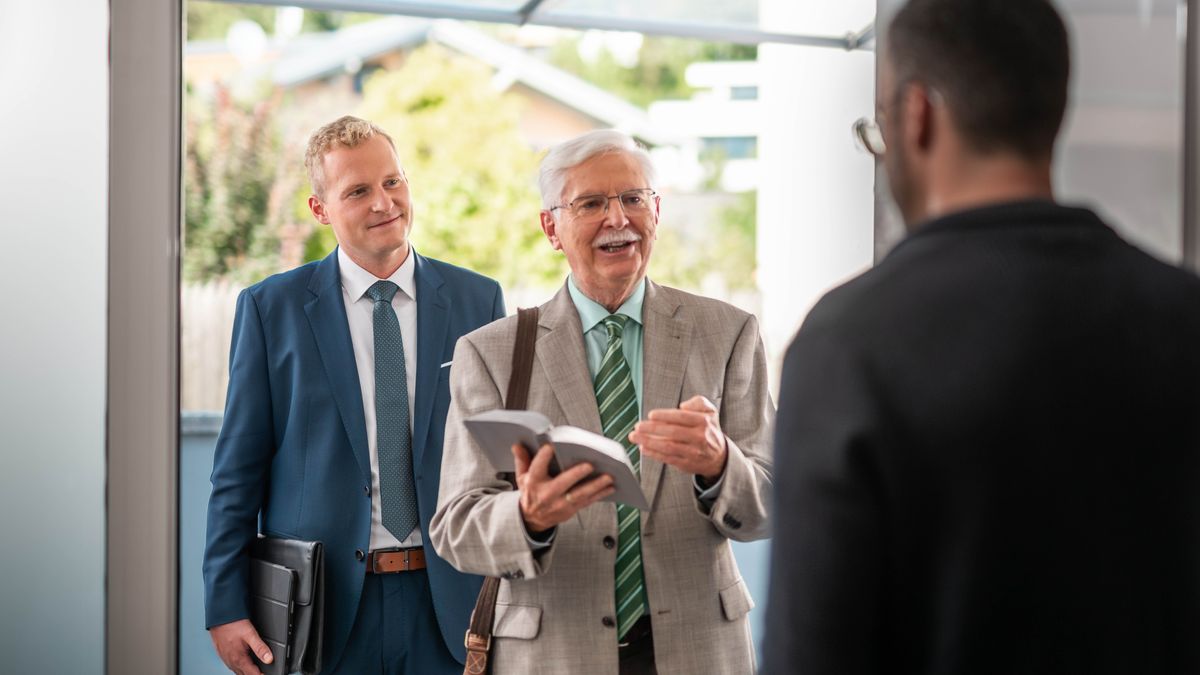 I due fratelli predicano insieme. Il fratello anziano, con convinzione, spiega un versetto a uomo sulla porta di casa.