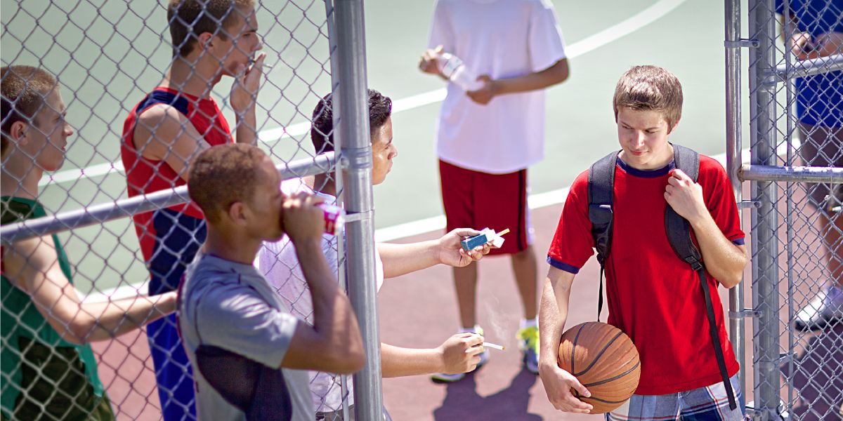 Un ragazzo a cui viene offerta una sigaretta dai compagni di scuola
