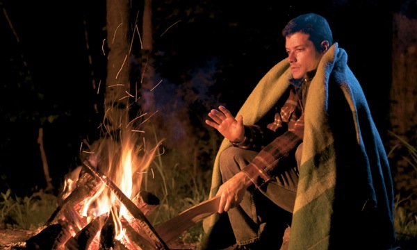 A man getting warm by a fire and adding wood to it