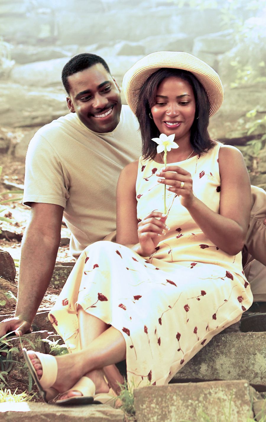 A husband and wife sit in a garden and admire a flower