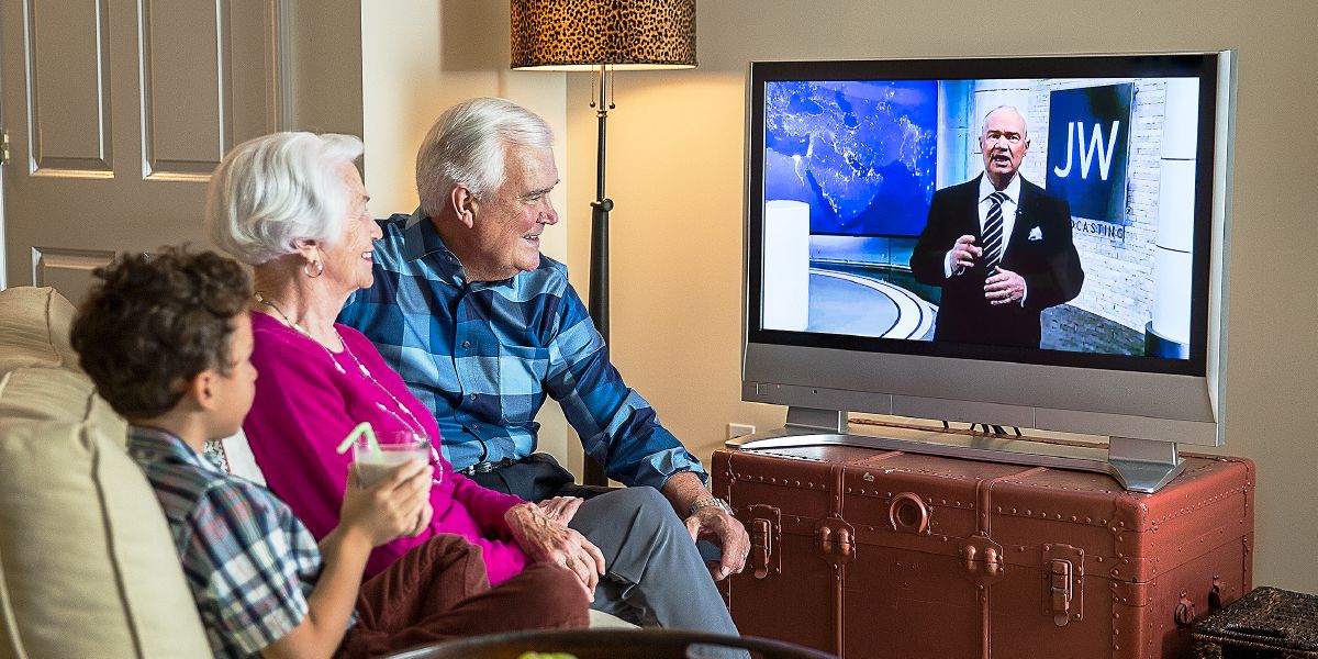 Егде жастағы ерлі-зайыпты мен кішкентай бала JW Broadcasting бағдарламасын тамашалап отыр