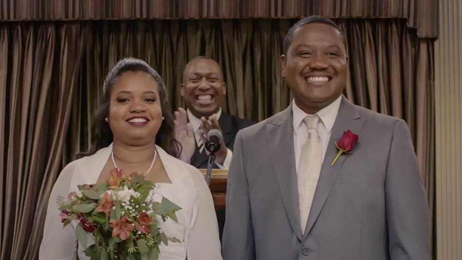 Picture from the video ‘Run Without Getting Tire​—Follow the Rules.’ Brother and Sister Calou smiling after their wedding talk to the Kingdom Hall.