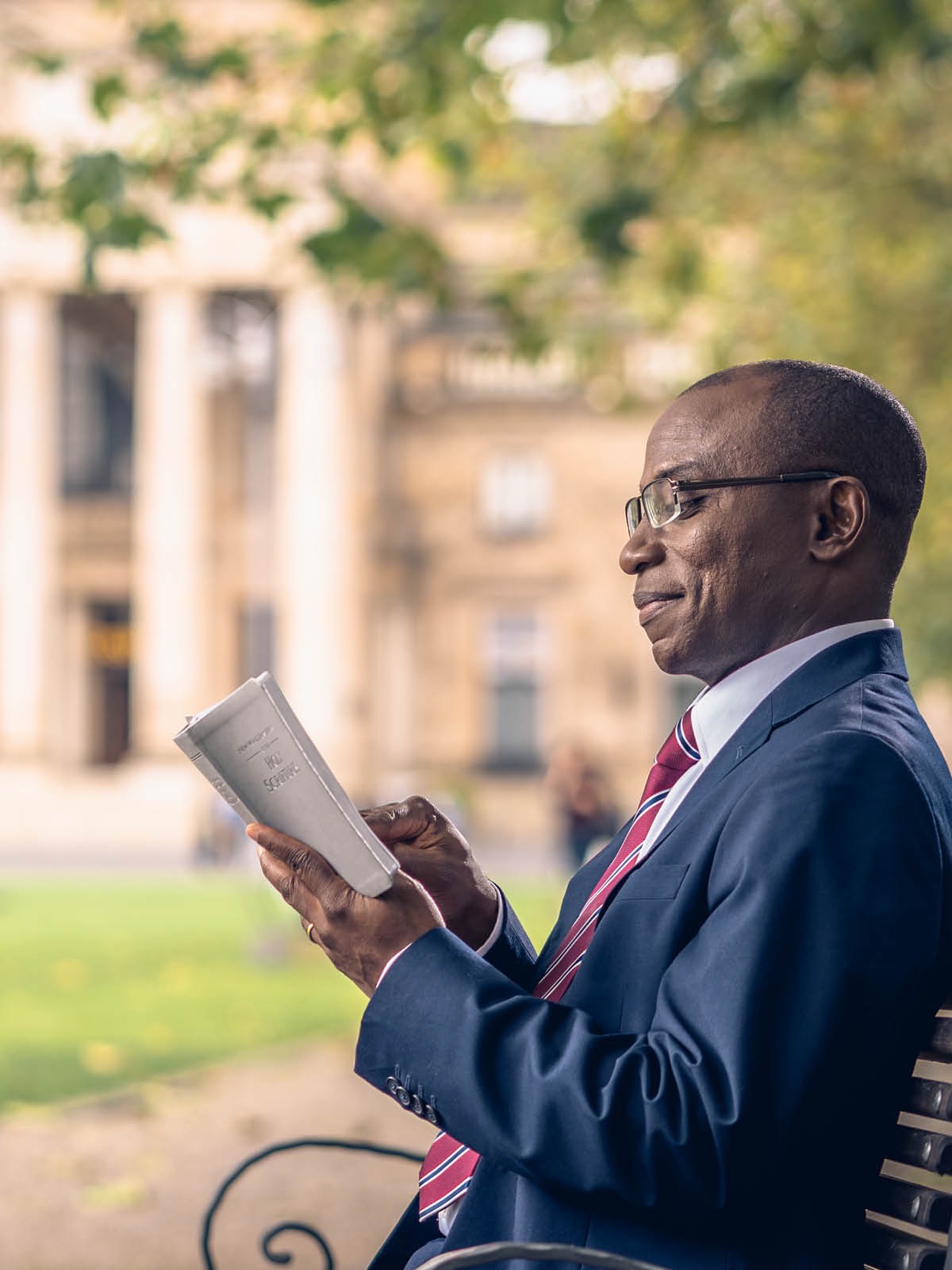 Moto moko afandi na kiti liboso ya ndako ya guvɛrnema mpe azali kotánga Biblia.