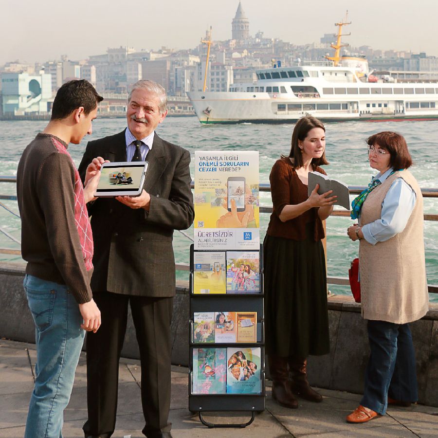 Jehovos liudytojai stovi prie literatūros stendo viešoje vietoje ir liudija praeiviams