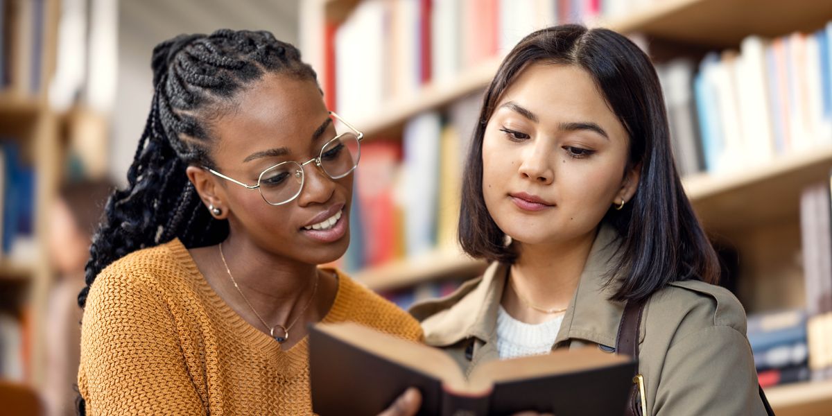 Divas jaunietes bibliotēkā lasa grāmatu.