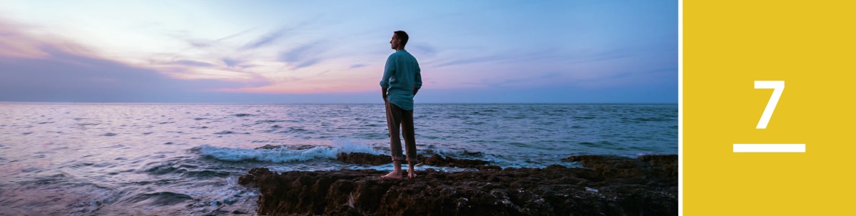 7. nodarbība. Vīrietis vakara krēslā stāv akmeņainā krastā un noraugās uz okeānu.