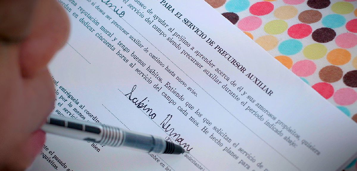 Savina Ernandesa tur mutē pildspalvu un aizpilda iesniegumu par palīgpioniera kalpošanu